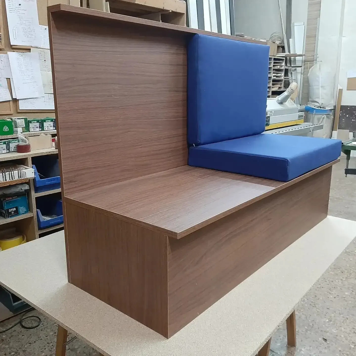 Banco de madera con asiento y respaldo acolchados en color azul, en entorno de taller.