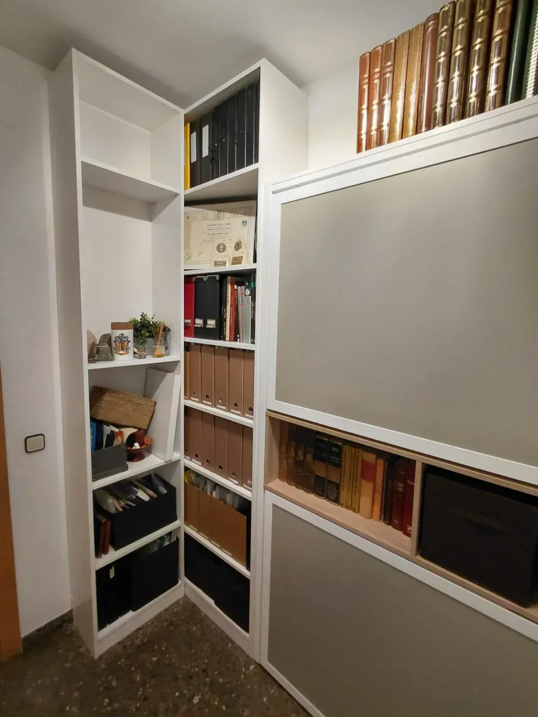 Estanterías blancas empotradas con diversos libros, archivos y artículos de decoración. 