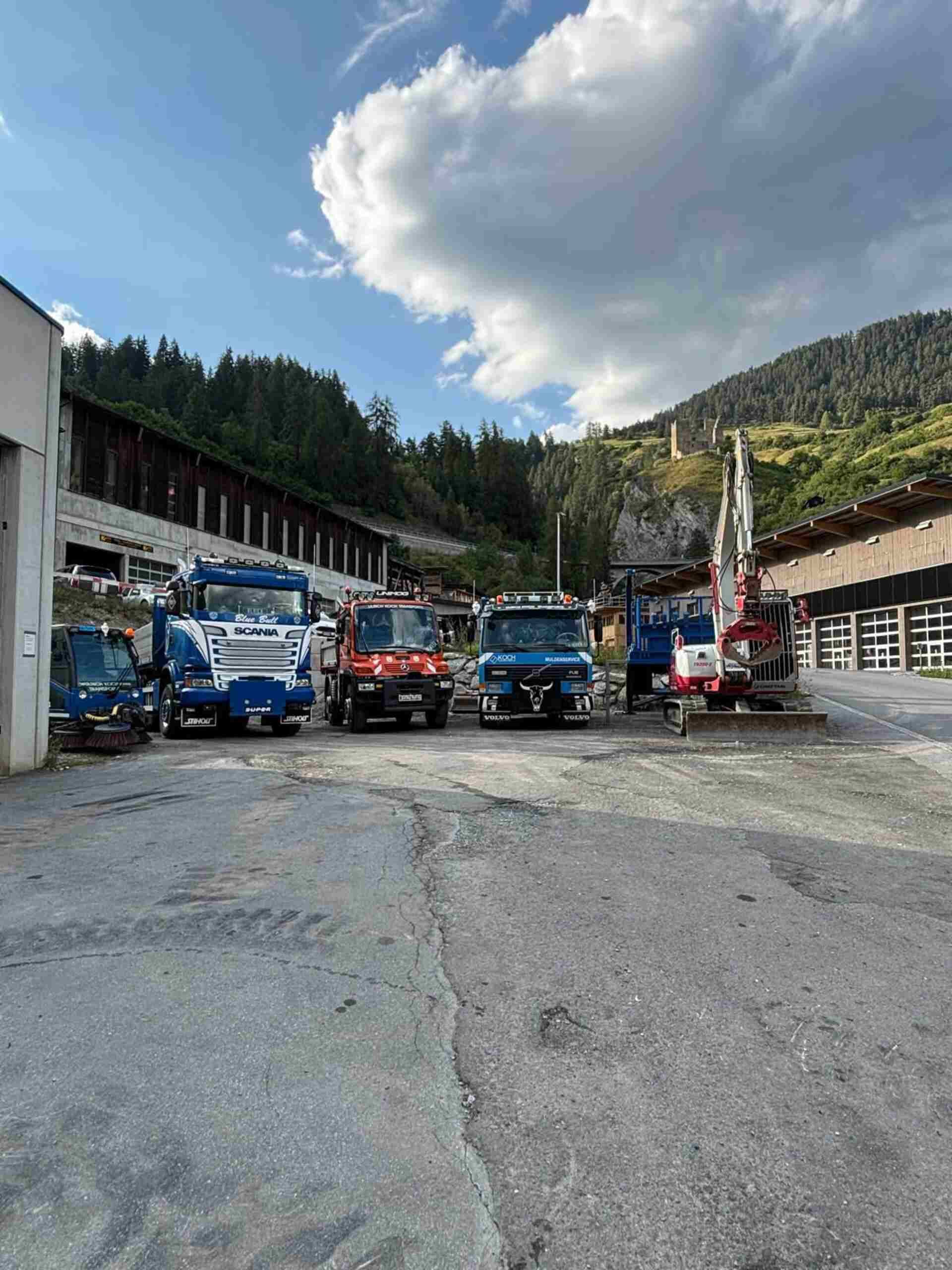 Auf einem Parkplatz vor einem Gebäude steht eine Reihe von Fahrzeugen von der Ulrich Koch Transporte GmbH.