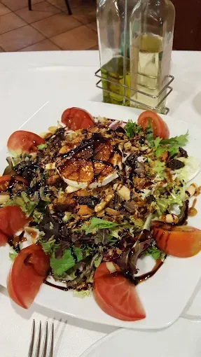 Ensalada con tomates, nueces y aderezo en un plato blanco; botellas de aceite y vinagre en el fondo.
