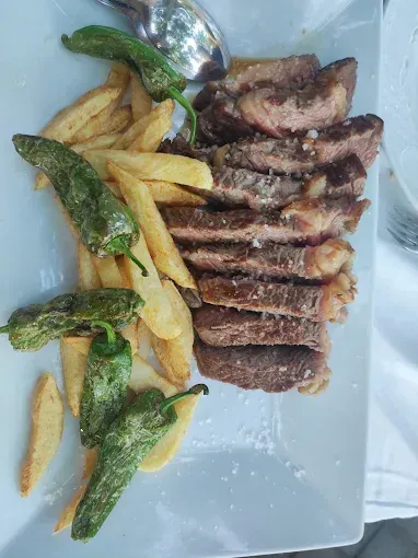 Filete en rodajas, patatas fritas y pimientos verdes en un plato blanco.