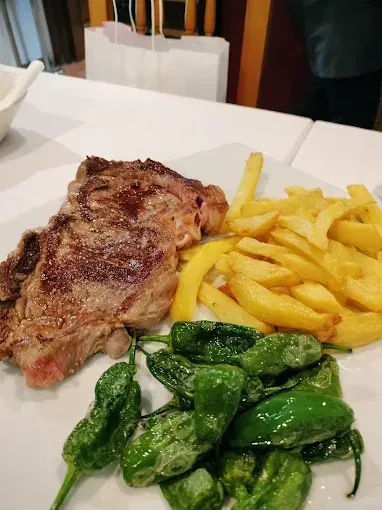 Filete, patatas fritas y pimientos verdes en un plato blanco. Ambiente de restaurante.