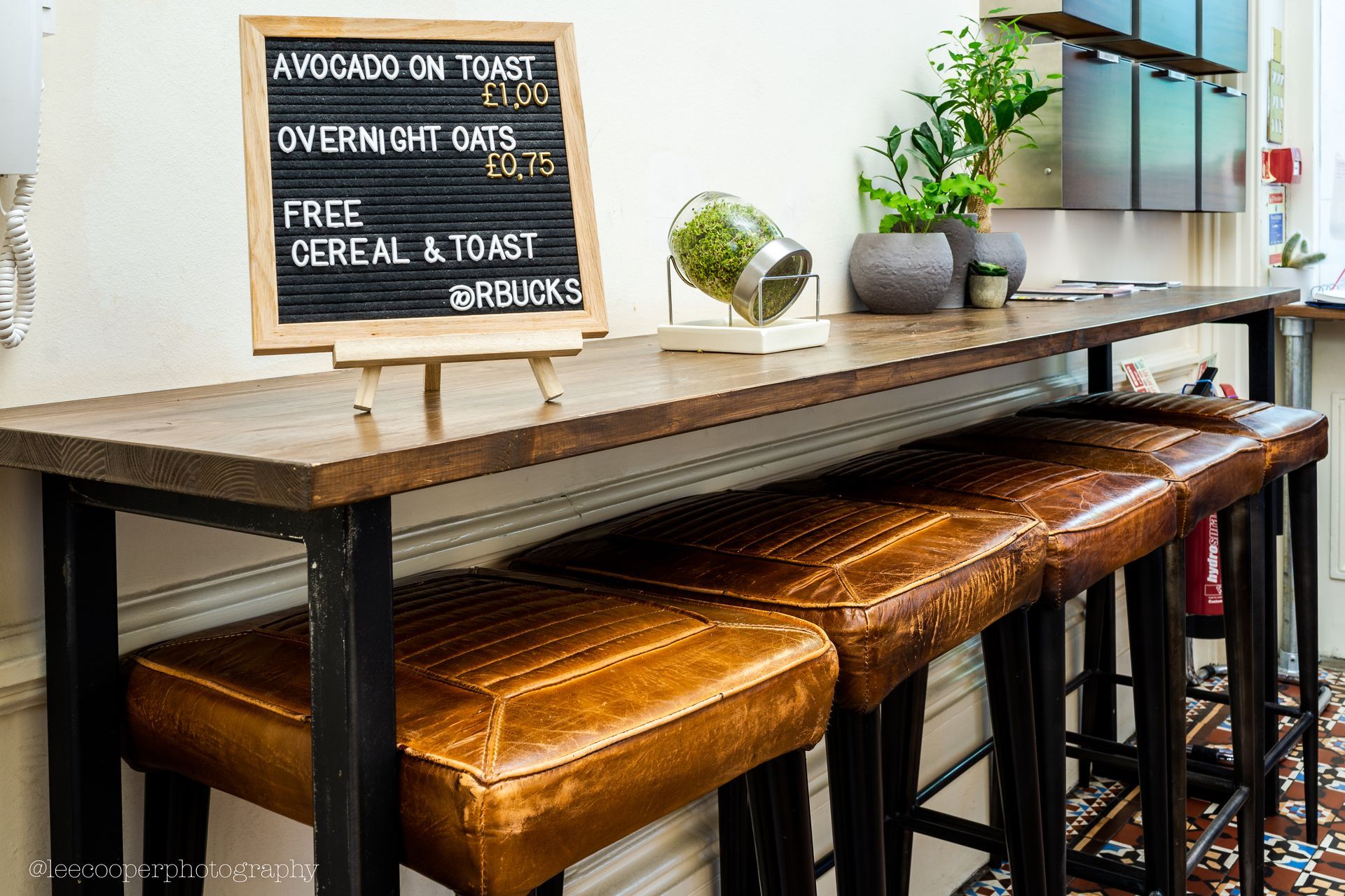 Wooden counter with leather stools, menu board: avocado toast, overnight oats, cereal & toast.