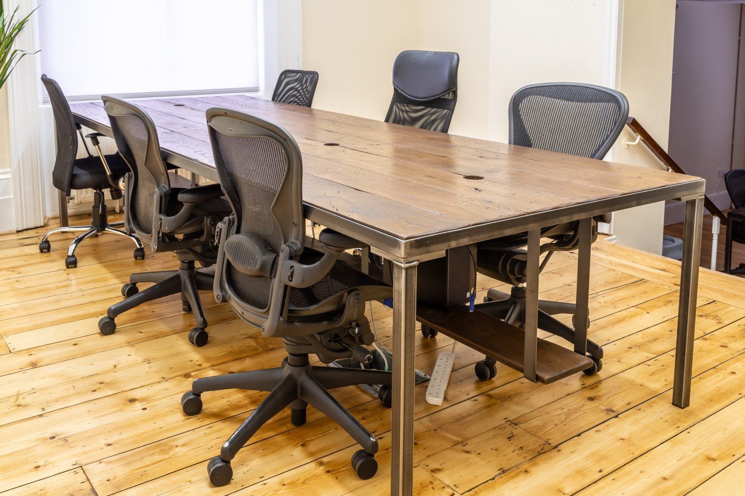 A conference table with six black office chairs on a light wood floor in an office.