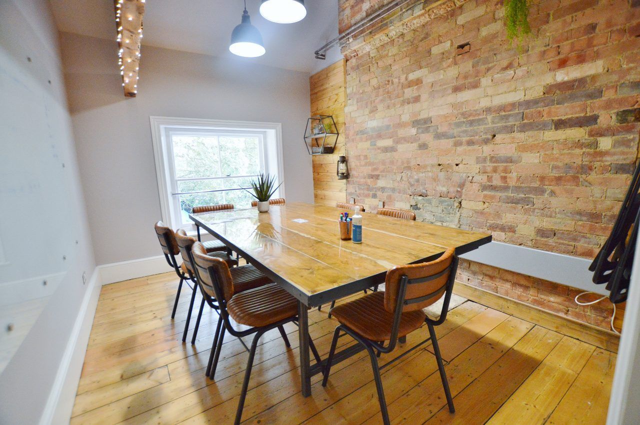 A dining area with a wooden table and chairs against a brick wall and window.