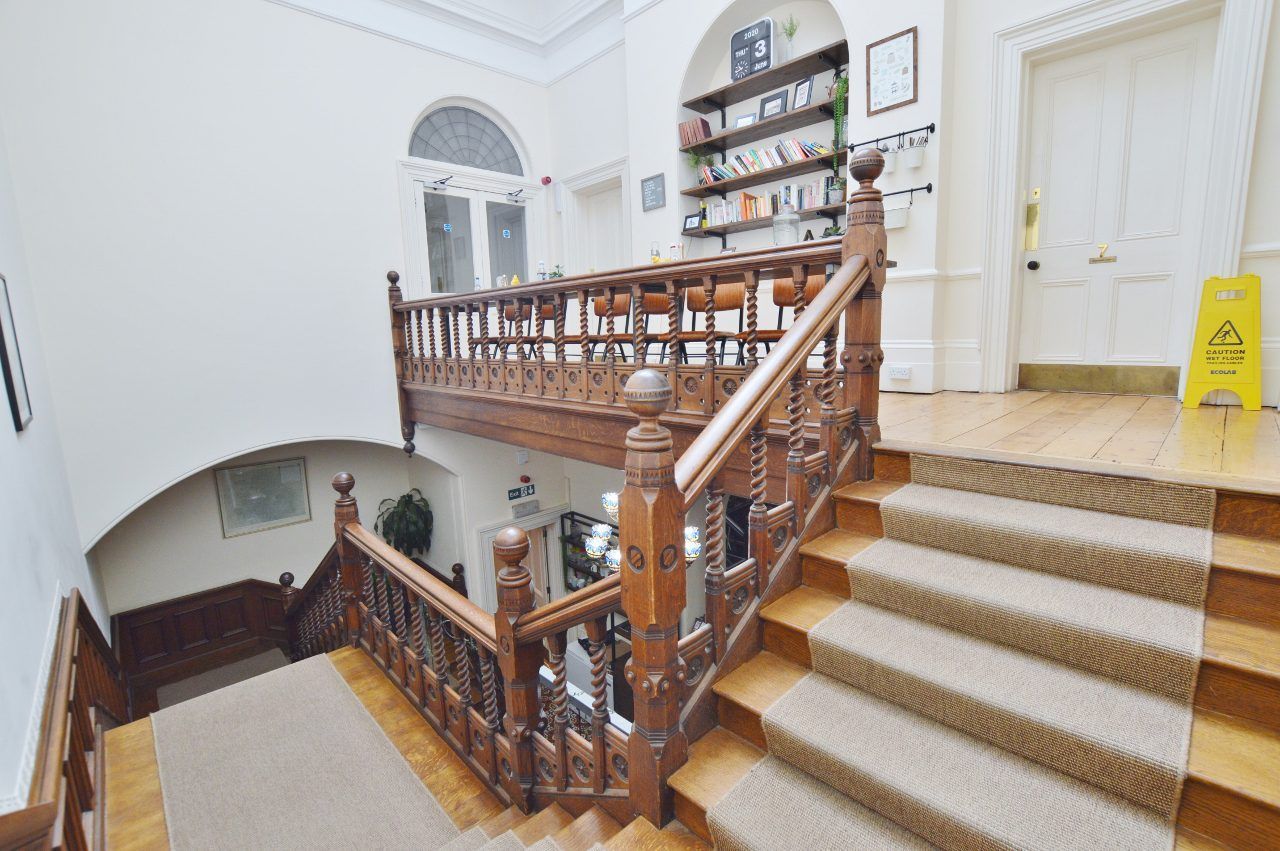 Wooden staircase with intricate railing, leading to a landing with bookshelves. Yellow