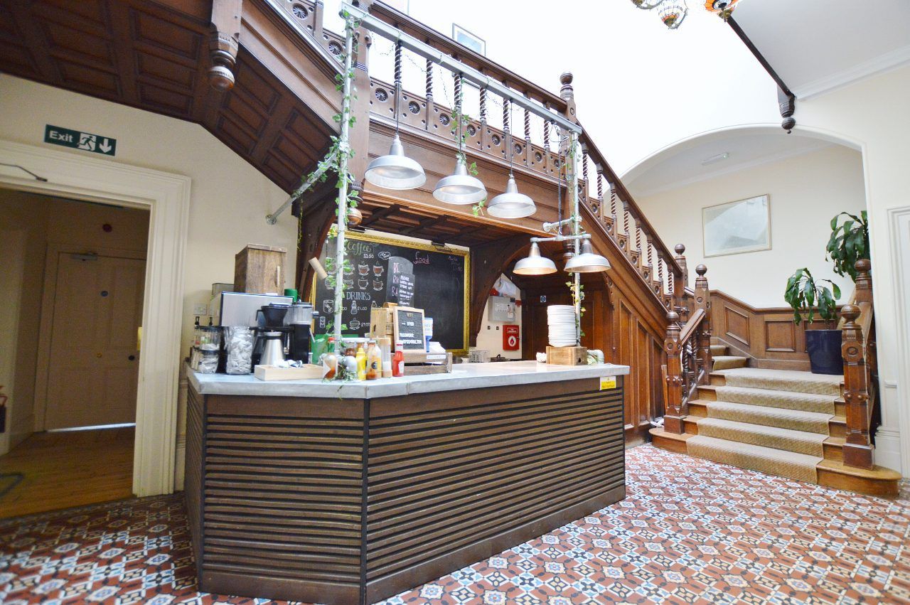 Cafe counter in ornate foyer with a wooden staircase and patterned floor.