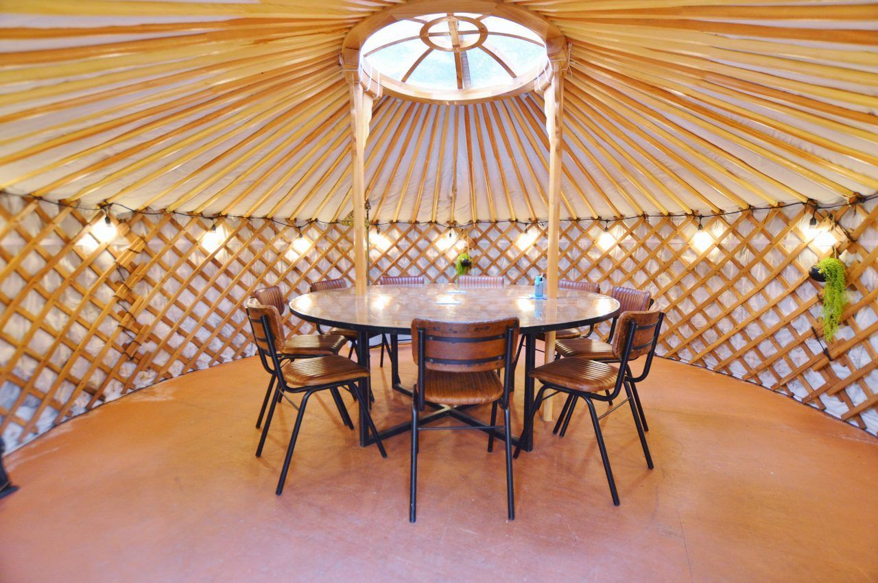 Inside a yurt with a round table and chairs, skylight overhead, and lattice walls.