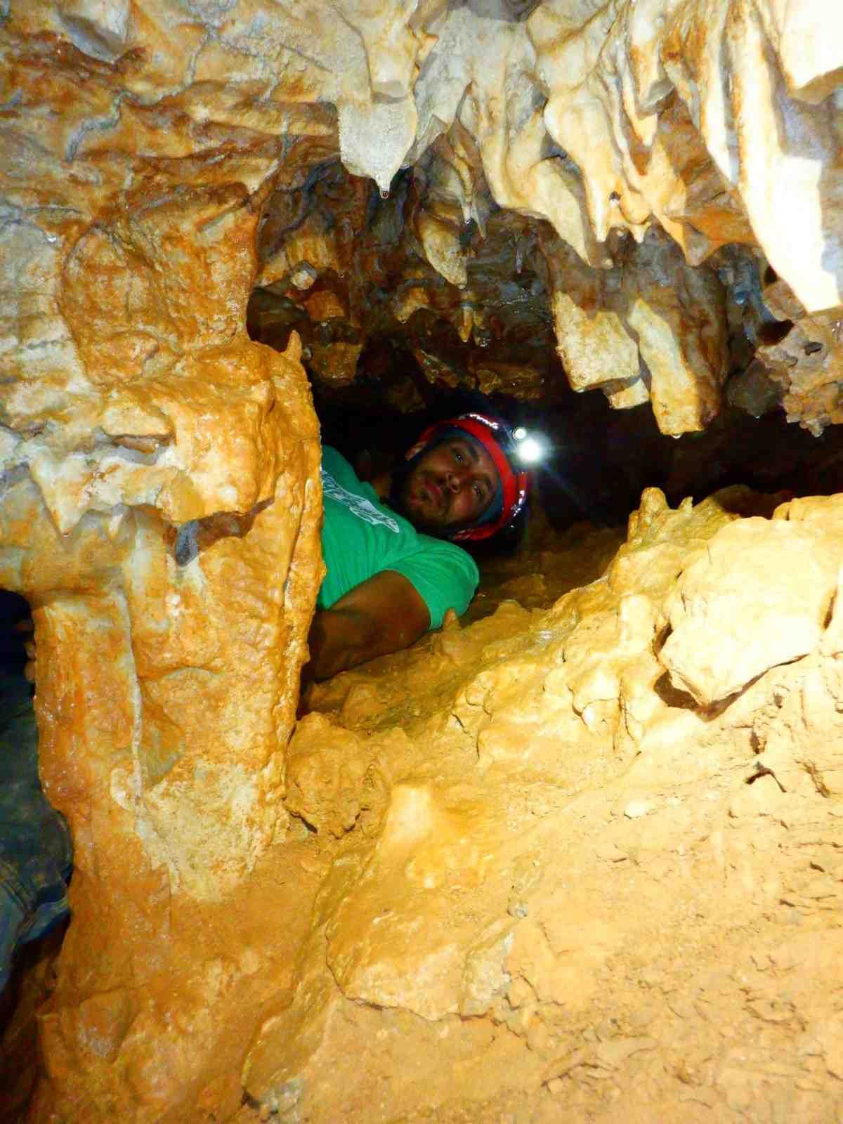 Una persona se arrastra por un estrecho pasaje de una cueva con una linterna frontal, rodeada de rocas.