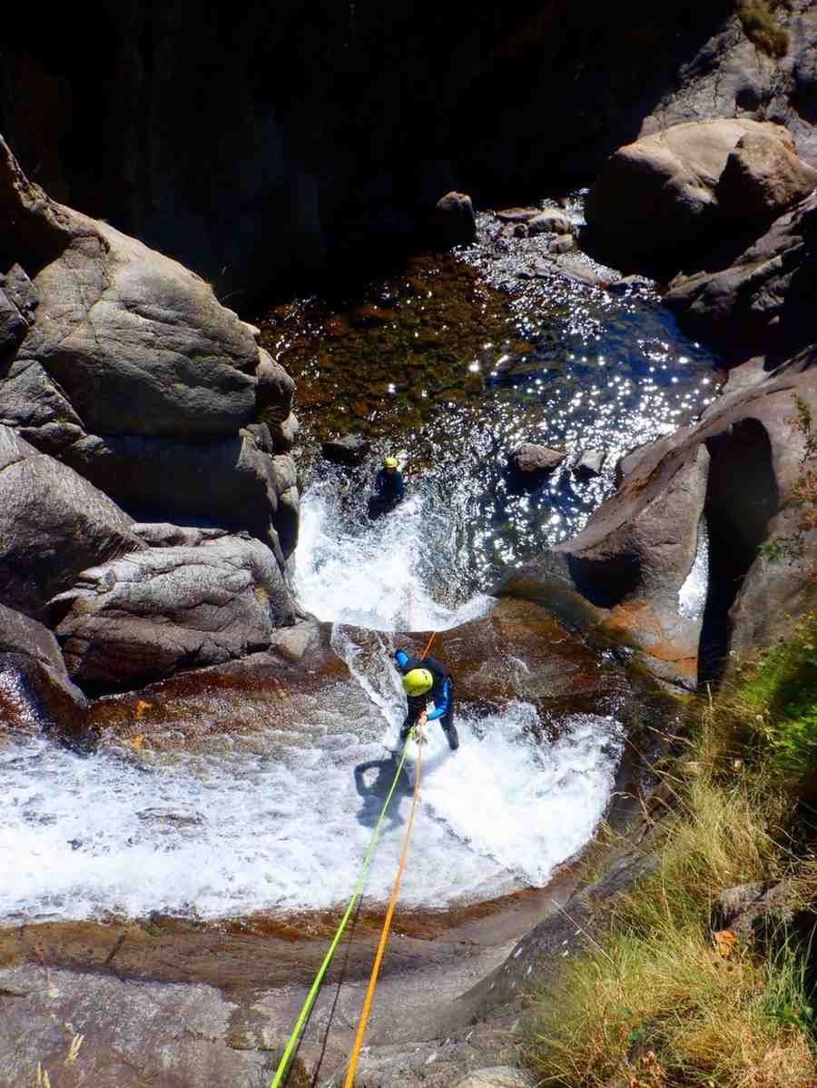 Descenso en rápel por un cañón rocoso y húmedo con una cuerda junto a una pequeña cascada.