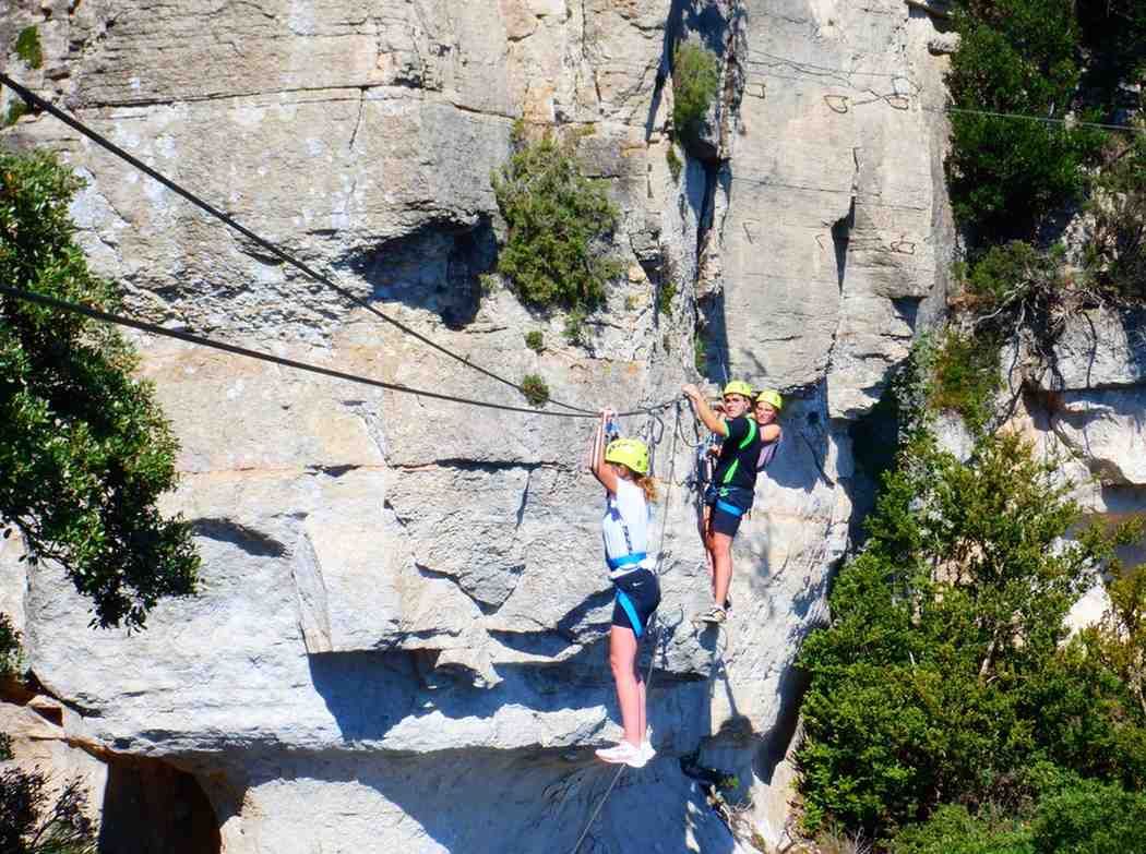Dos escaladores con cascos ascienden una empinada pared de roca con cuerdas y arneses.