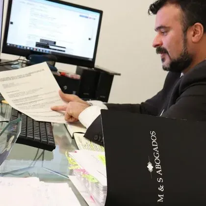 Un hombre sentado en un escritorio con un libro que dice M & S Abogados