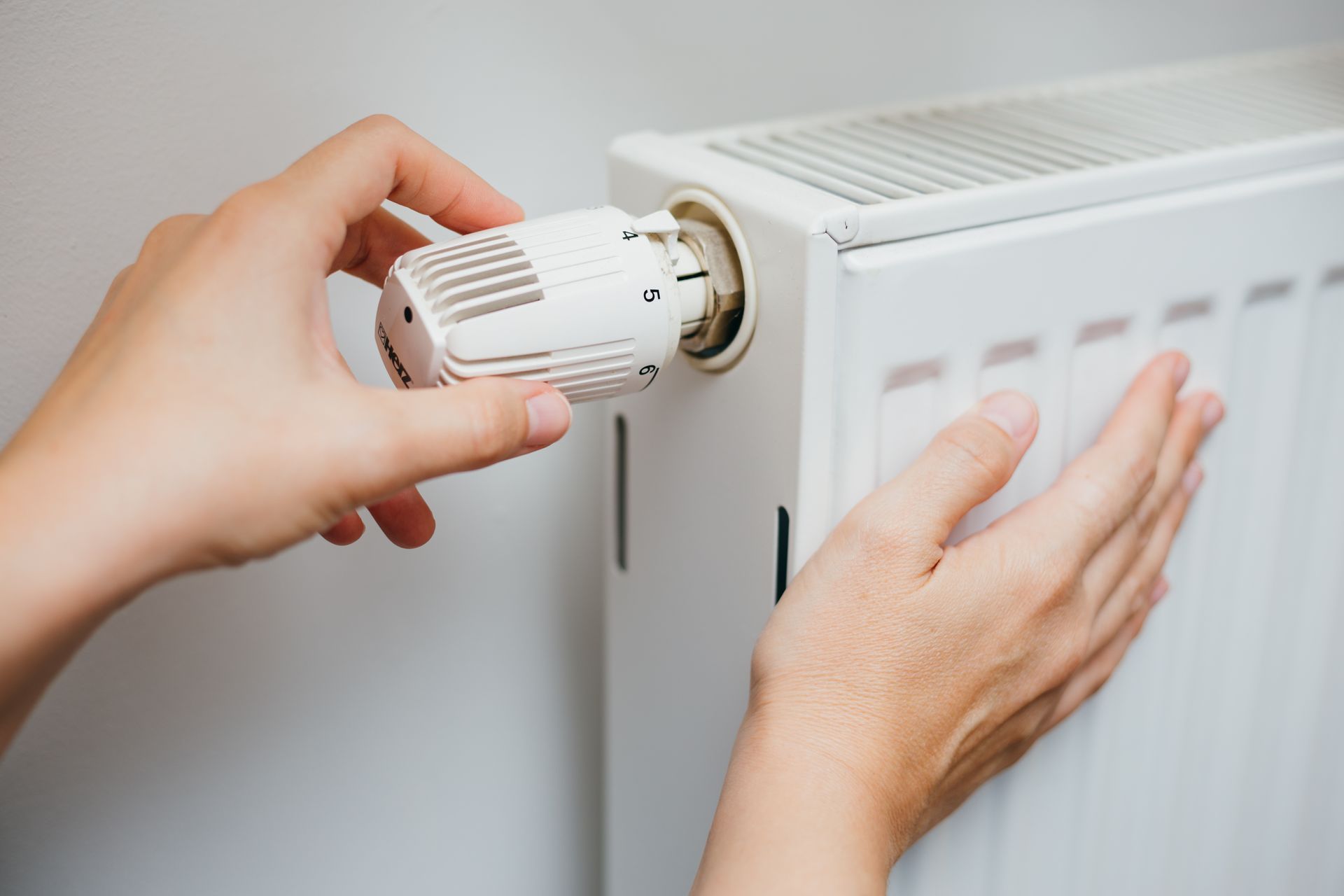 Des mains règlent le thermostat d'un radiateur blanc.