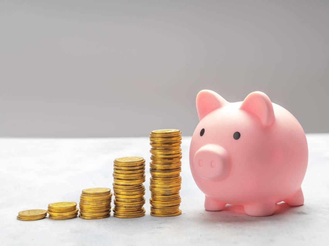 Une tirelire rose à côté de piles de pièces d'or, symbolisant l'épargne et la croissance.