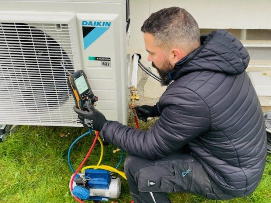 Un homme effectue la maintenance d'un climatiseur Daikin à l'extérieur, à l'aide de manomètres et d'une pompe à vide.
