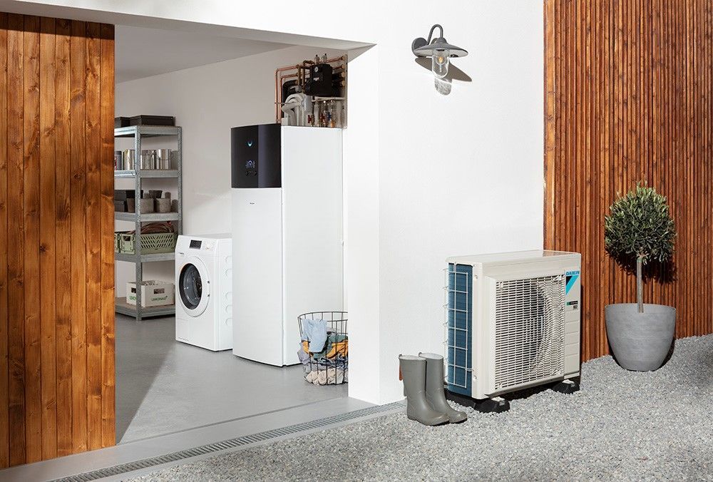 Une pompe à chaleur extérieure jouxte une buanderie blanche équipée d'un lave-linge et d'espaces de rangement.