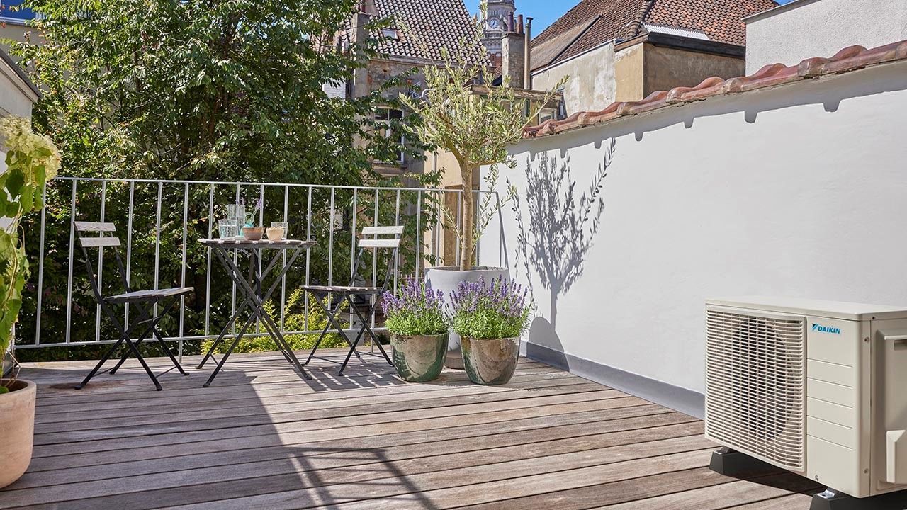 Terrasse avec petite table et chaises, plantes en pot et un climatiseur blanc.