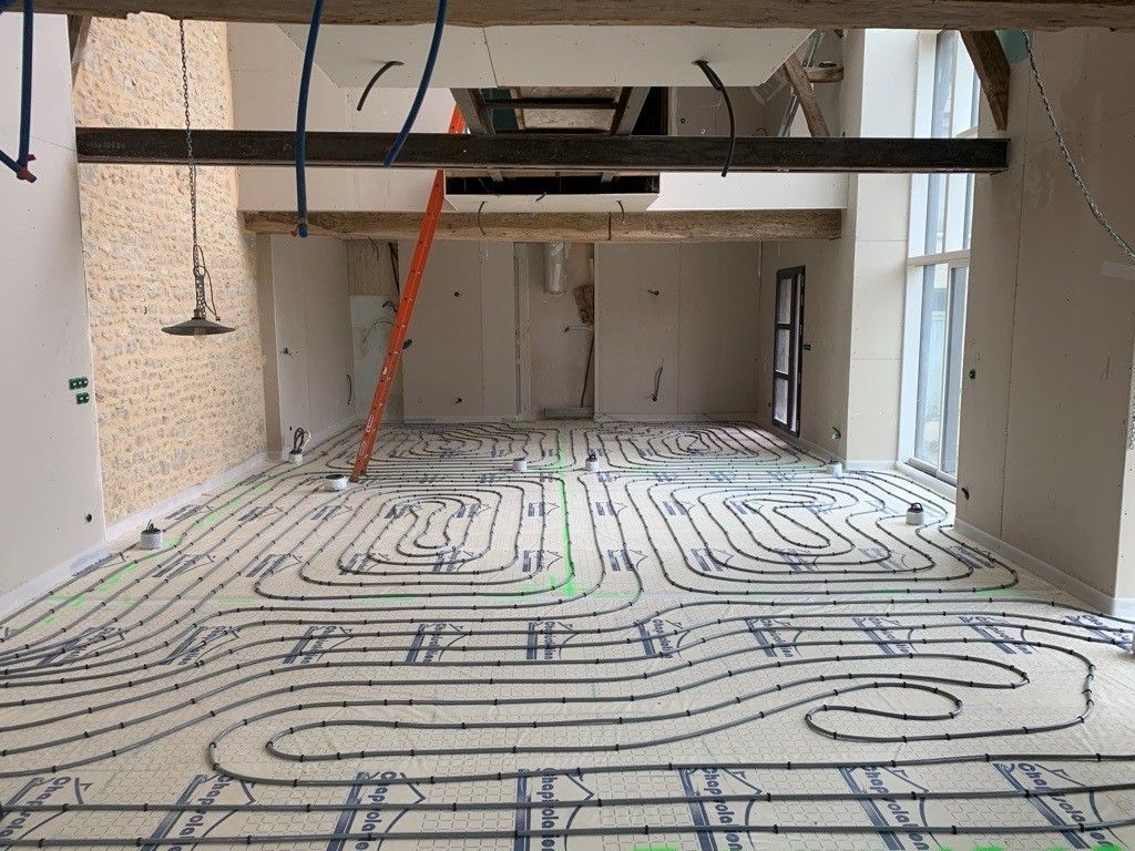 Pièce équipée d'un système de chauffage au sol radiant, prête à recevoir le revêtement de sol. Tubes noirs sur une surface blanche.