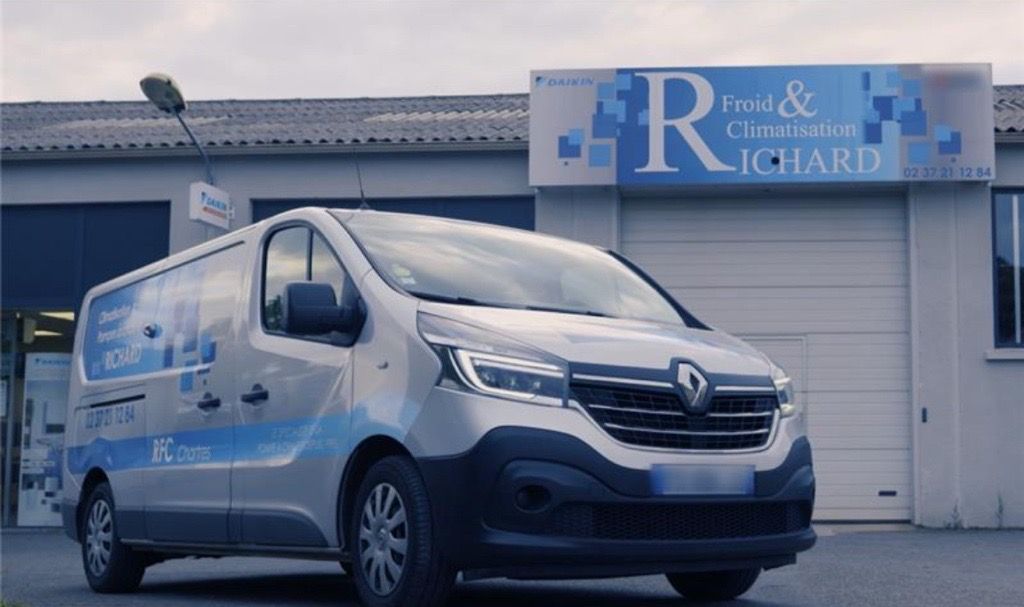 Fourgonnette Renault argentée garée devant un bâtiment avec une pancarte