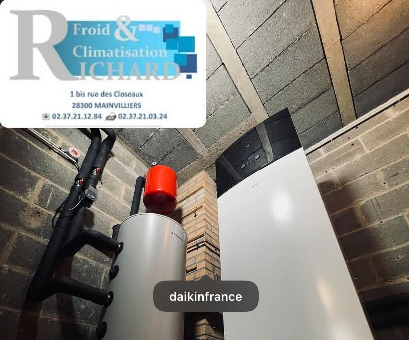 Équipement installé par Richard pour Froid & Climatisation. Réservoir blanc à couvercle rouge, tuyaux noirs, contre un mur de briques.