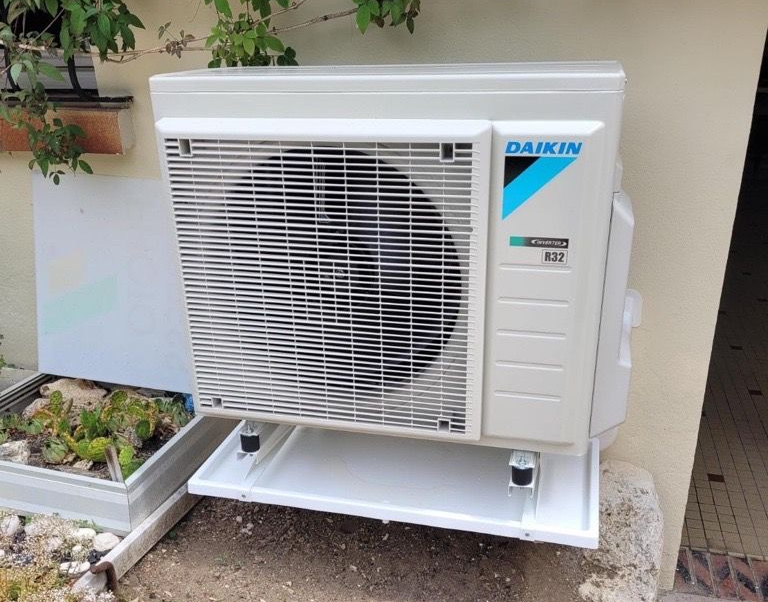 Unité de climatisation Daikin fixée sur un support à l'extérieur, contre un mur.