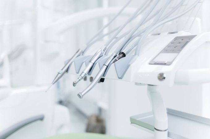 Sillones de clínica dental con instrumental colgado en una sala de tratamiento de color blanco brillante.