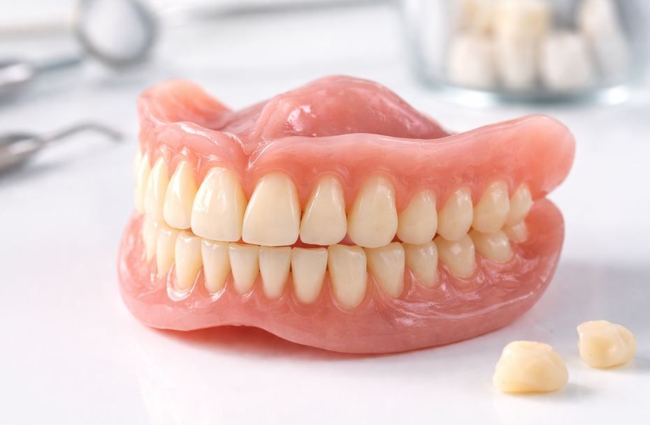 Prótesis dentales artificiales sobre una superficie blanca, con dos piezas de dientes sueltos cerca.