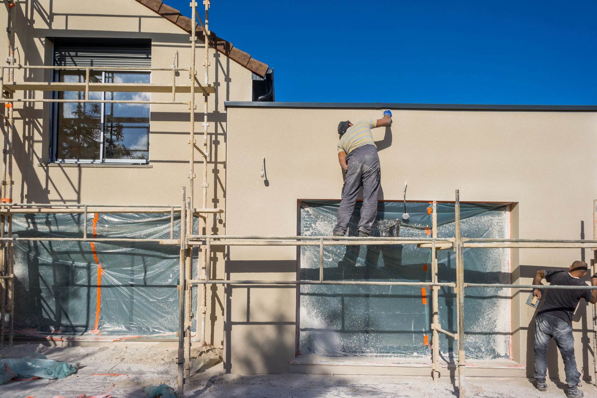 Un ouvrier sur un échaffaudage en train de peindre le mur extérieur d'une maison