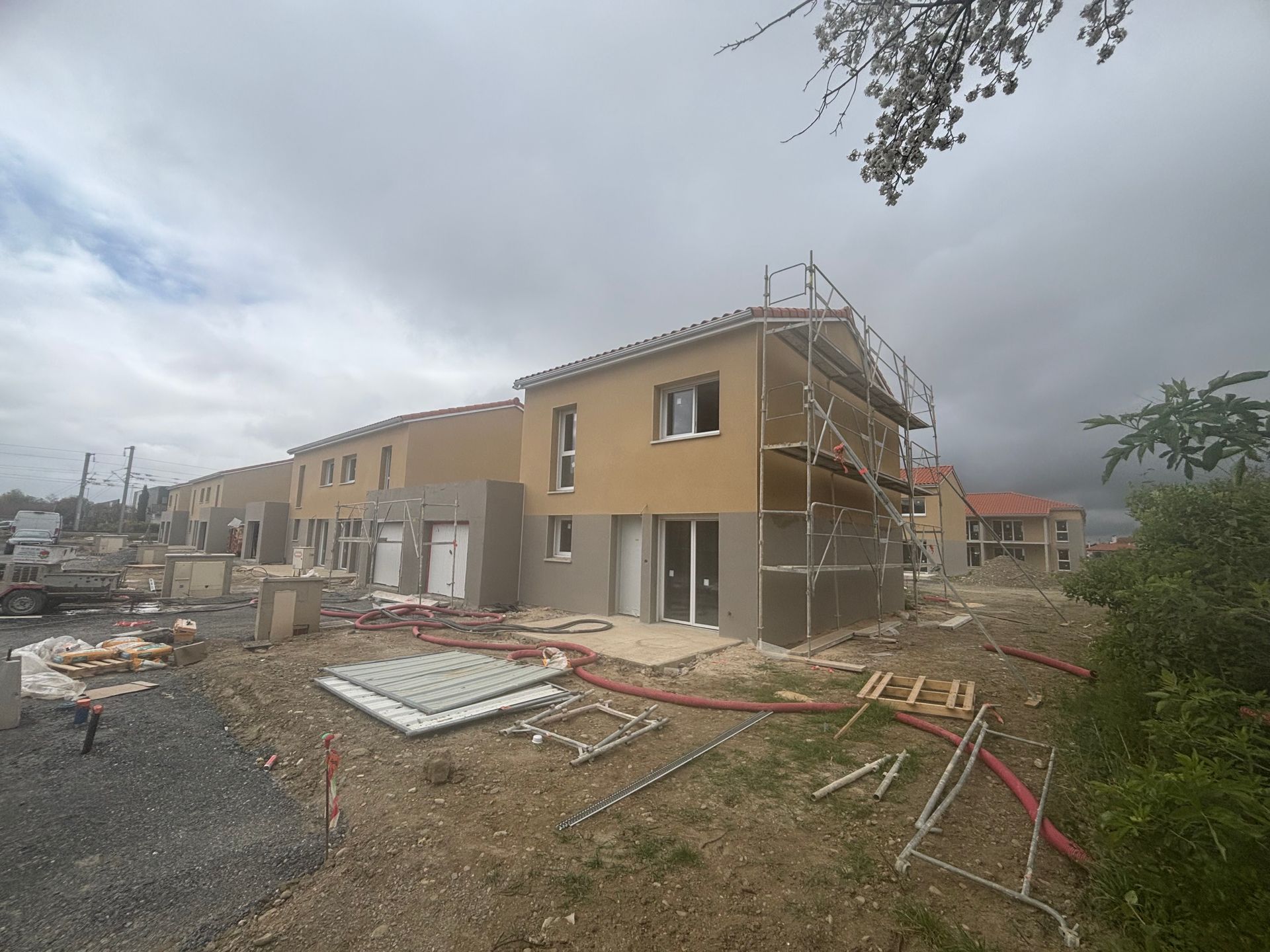 Un chantier de construction montrant des maisons de ville résidentielles de deux étages aux façades beiges et grises sous un ciel nuageux.