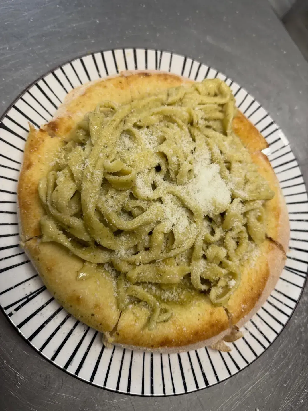 Plato de pasta: Pasta verde sobre una base de masa horneada, espolvoreada con queso, servida en un plato a rayas.