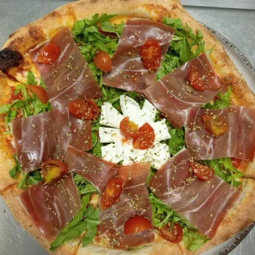 Pizza con prosciutto, rúcula, tomates cherry y mozzarella.
