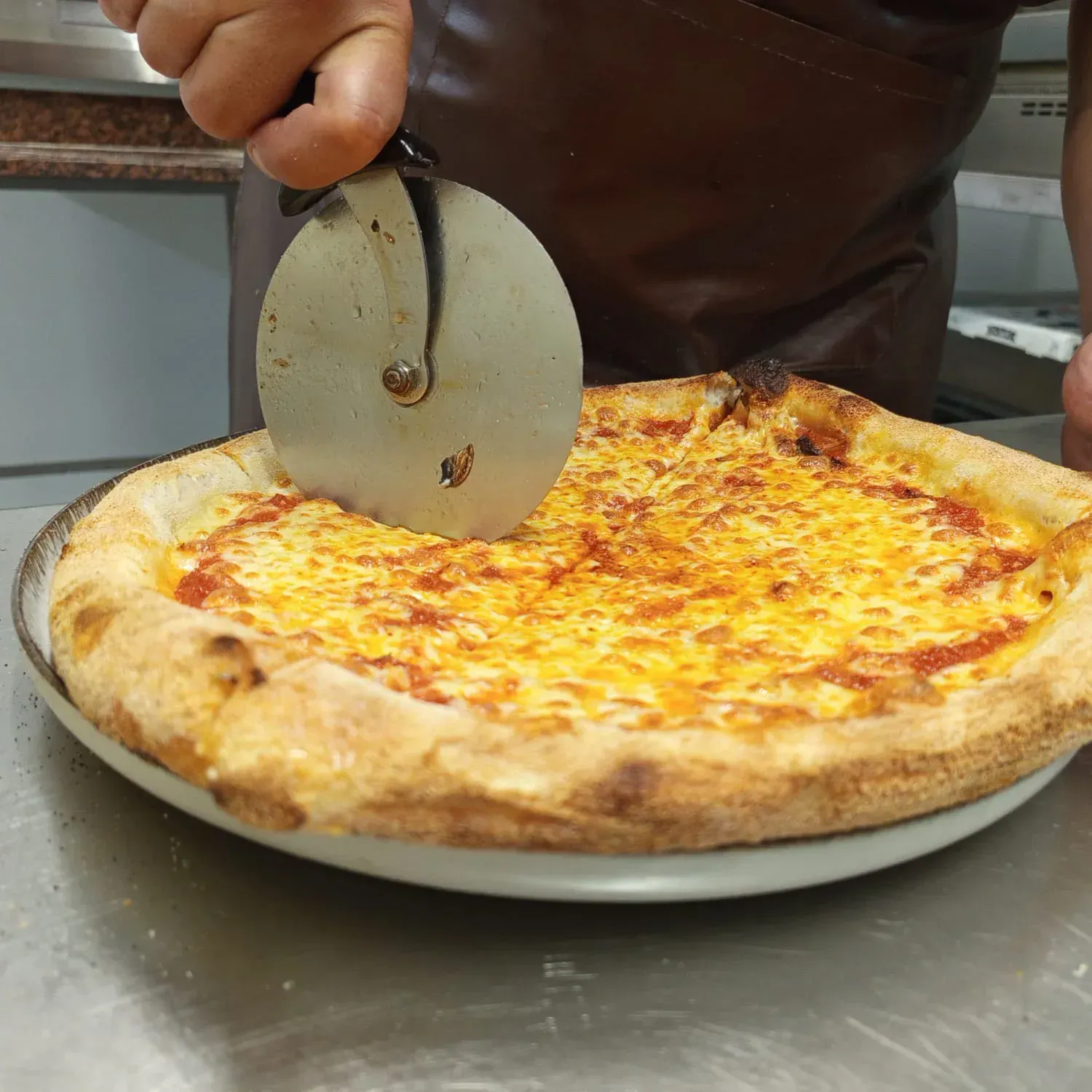 Se está cortando una pizza con un cortador de pizza, sobre un plato.