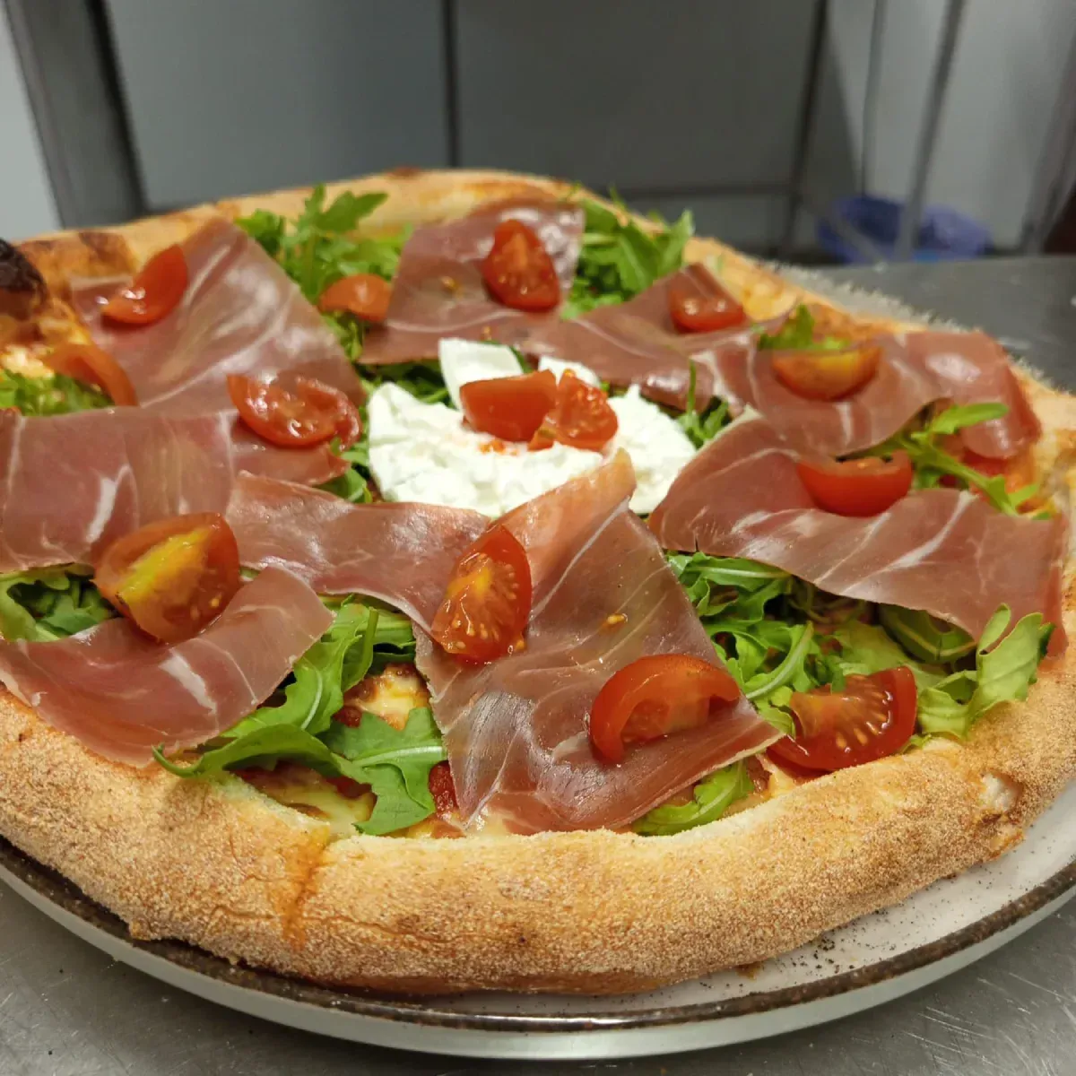Pizza con prosciutto, rúcula, tomates cherry y queso burrata.
