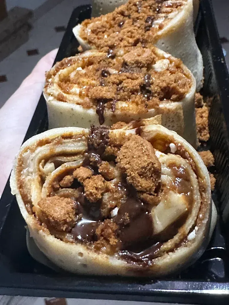 Rollitos de crepa cubiertos con migas de galleta y salsa de chocolate.