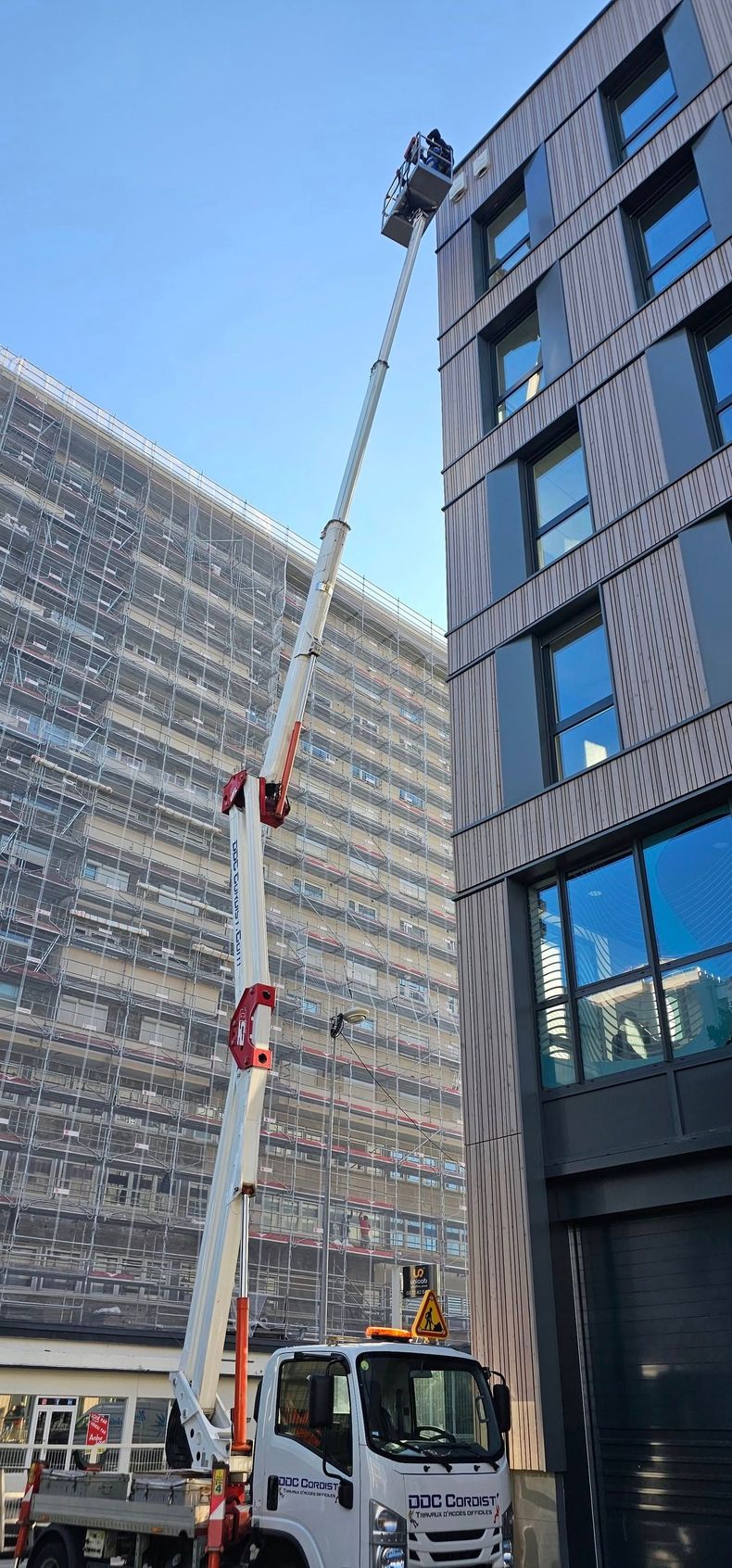 Grue soulevant un ouvrier à côté d'un immeuble moderne dans une rue de la ville