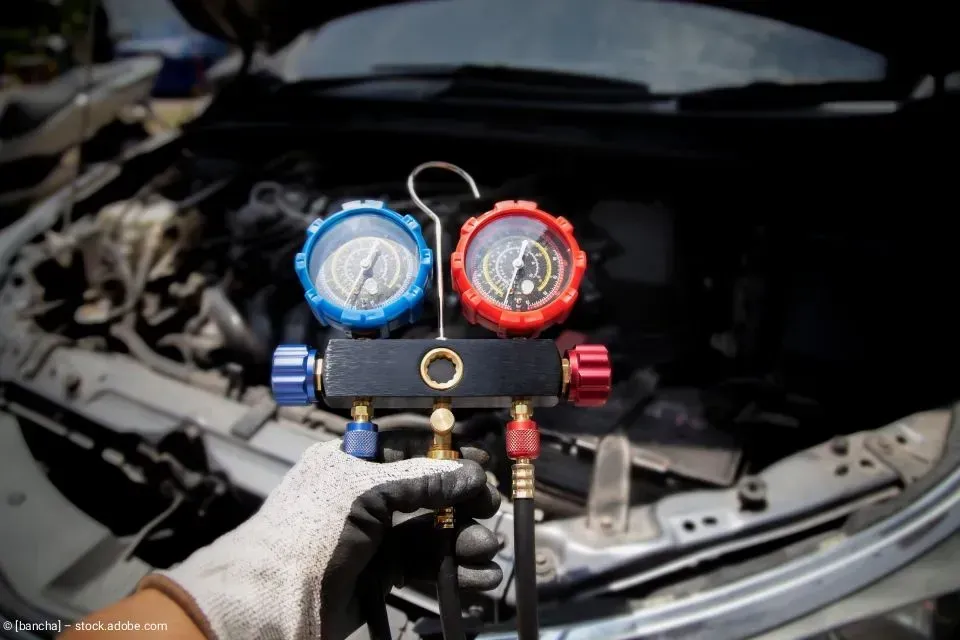 Ein Mechaniker schließt Messgeräte an die Klimaanlage eines Autos unter der Motorhaube an.