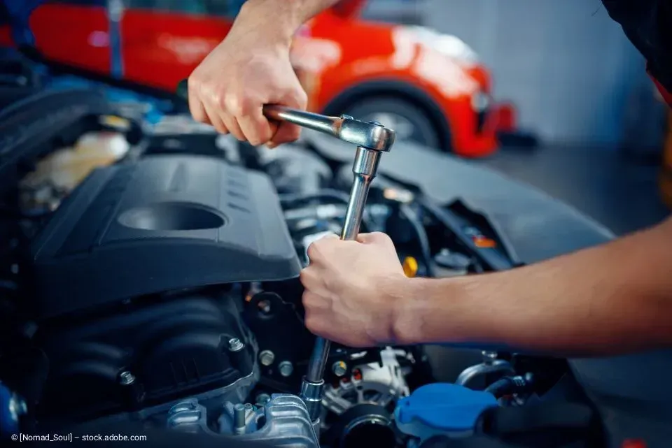 Hände benutzen einen Schraubenschlüssel, um in einer Garage einen Automotor zu reparieren