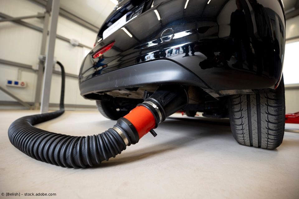 Schwarzes Auto mit einem roten Auspuffadapter, der an einen Wellschlauch angeschlossen ist, in einer Garage