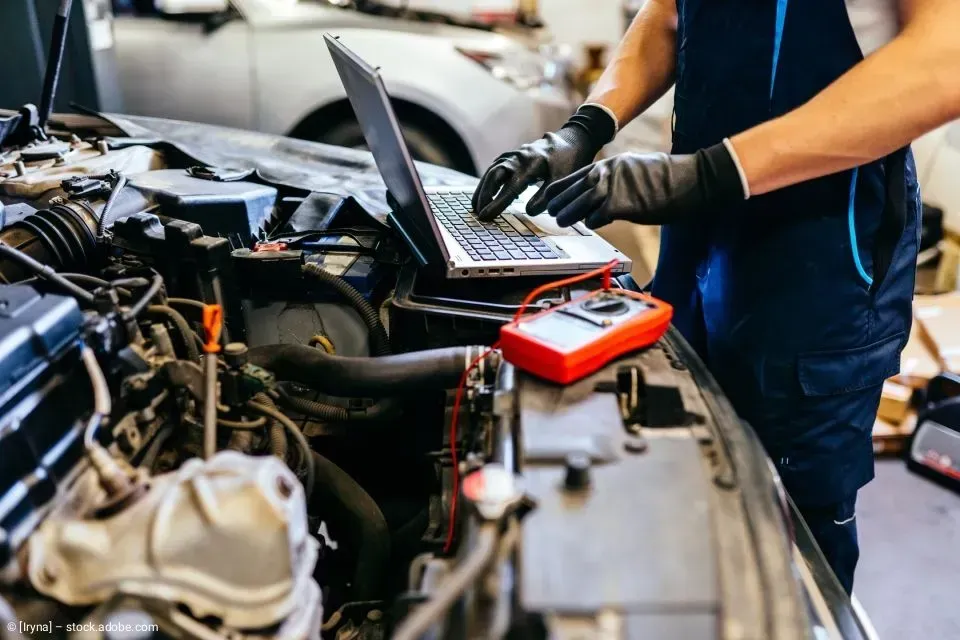 Ein Mechaniker benutzt in einer Werkstatt einen Laptop und ein Diagnosegerät an einem Automotor.