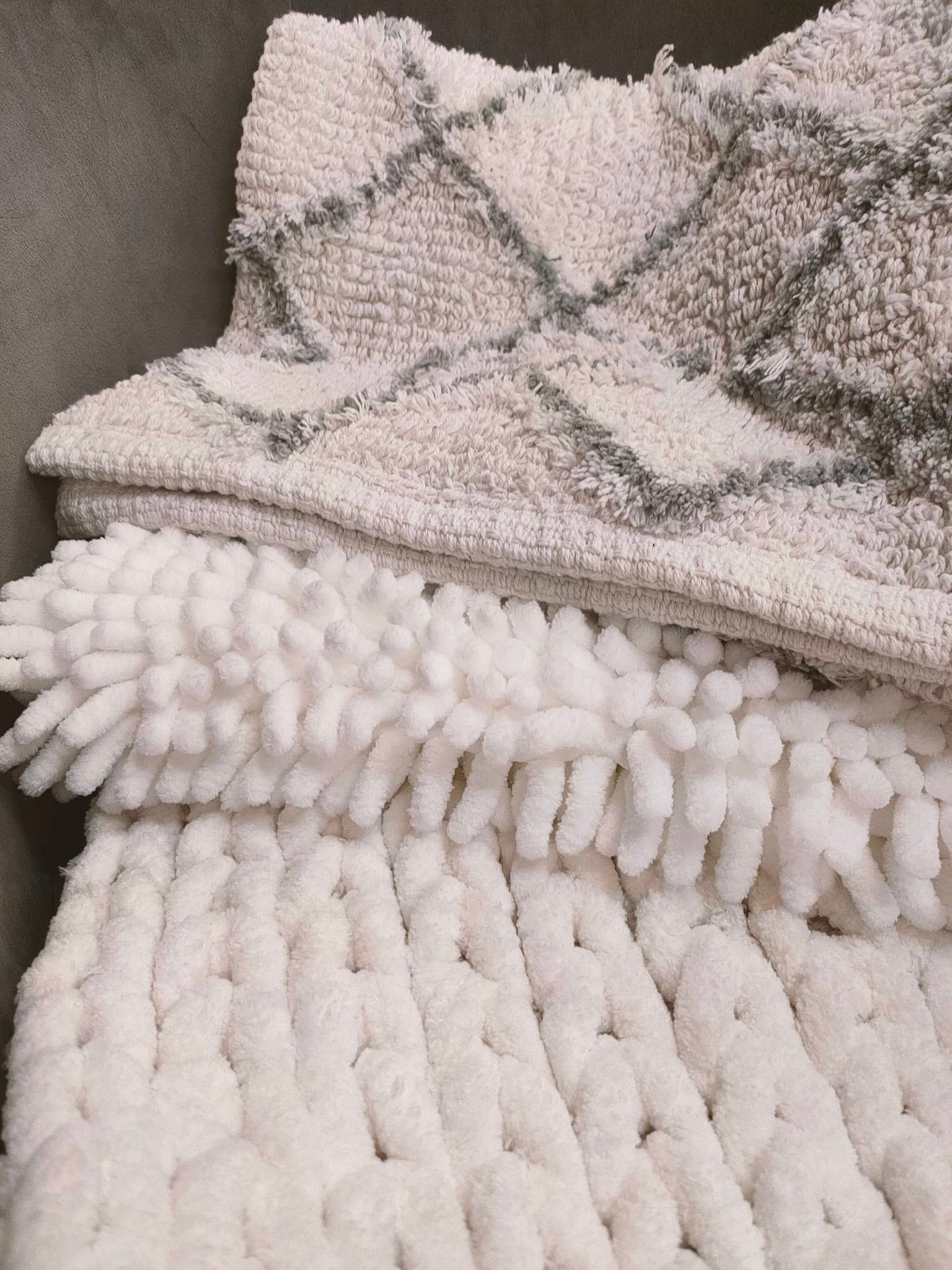 Des tapis de bain texturés blancs et gris superposés avec des motifs géométriques.