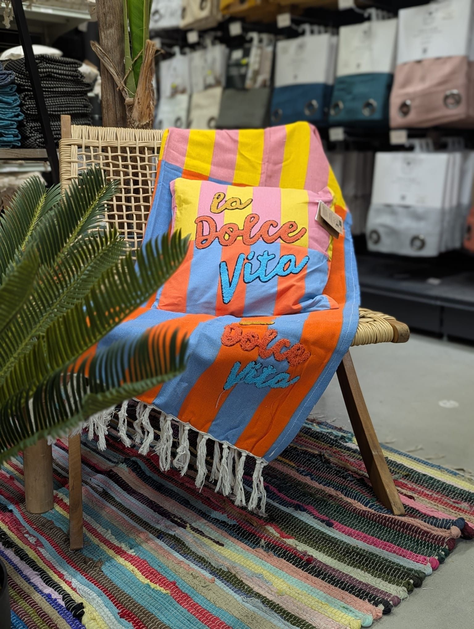 Fouta et coussin avec des rayures bleues, rouges, jaunes et roses sur une chaise en osier.