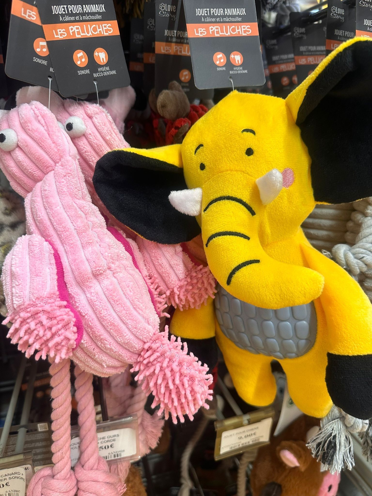 Des peluches roses et jaunes pour animaux suspendues sont présentées sur une étagère de magasin.