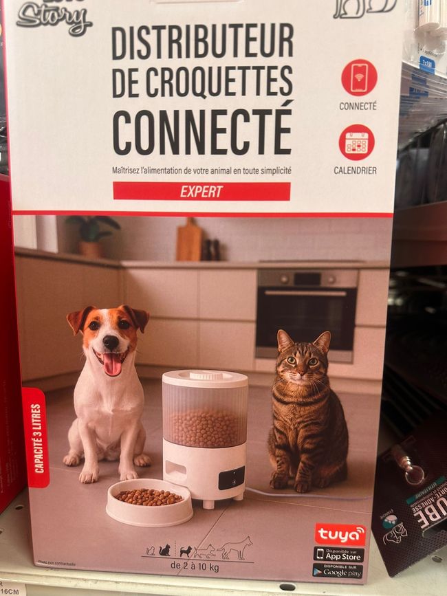 Boîte d’un distributeur de croquettes connecté avec un chien et un chat devant dans une cuisine.