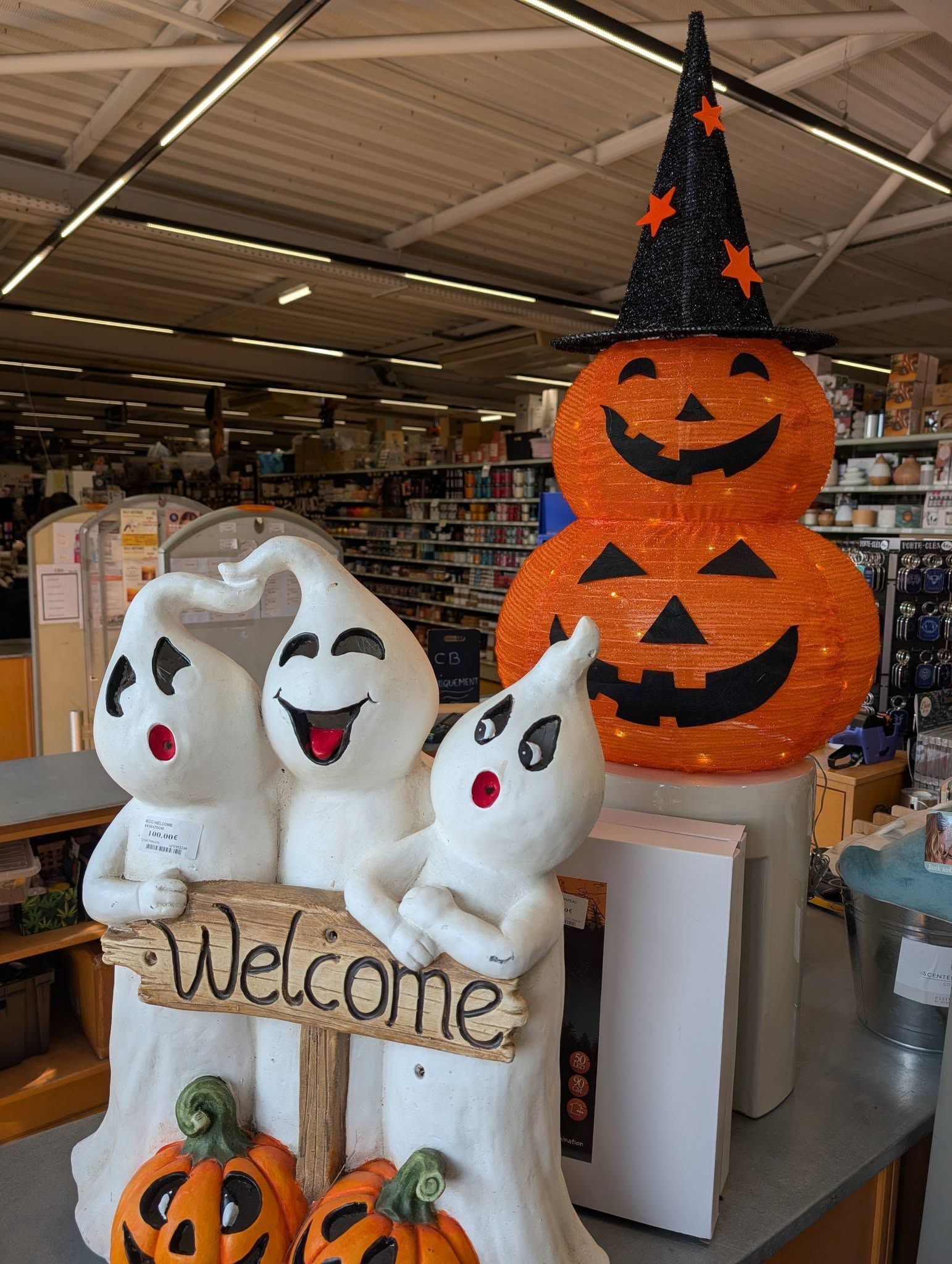 Décoration d'Halloween avec des figurines de fantômes, des citrouilles et un panneau portant l'inscription Bienvenue.