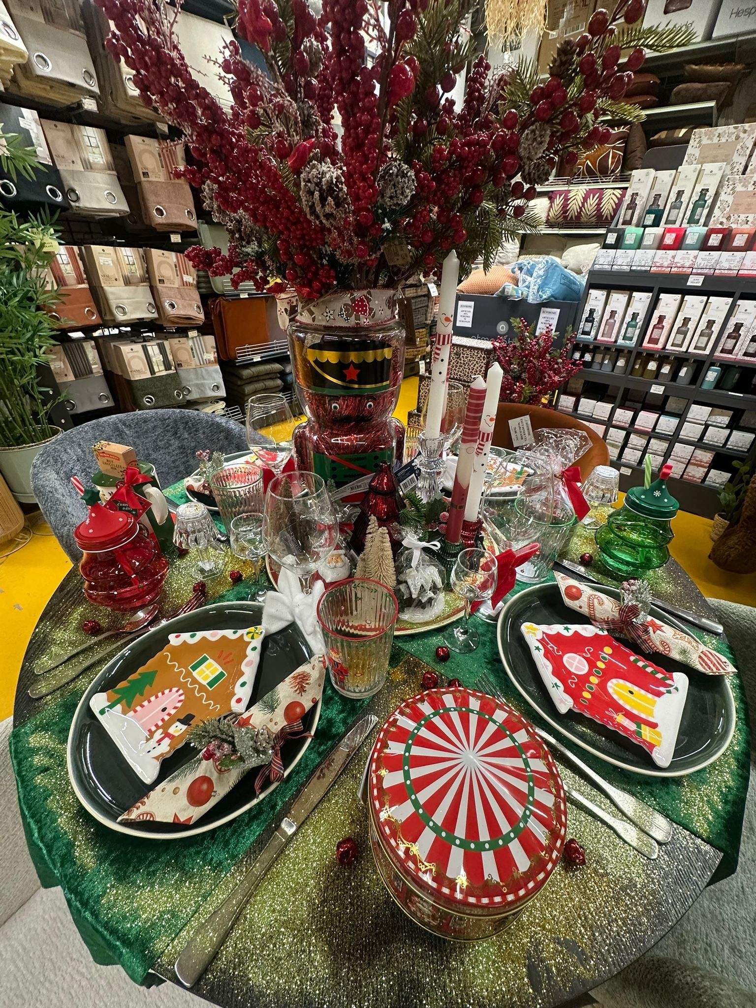 Décoration festive de Noël avec des ornements rouges et verts, des plateaux de cadeaux et un petit sapin décoré dans une allée de magasin.