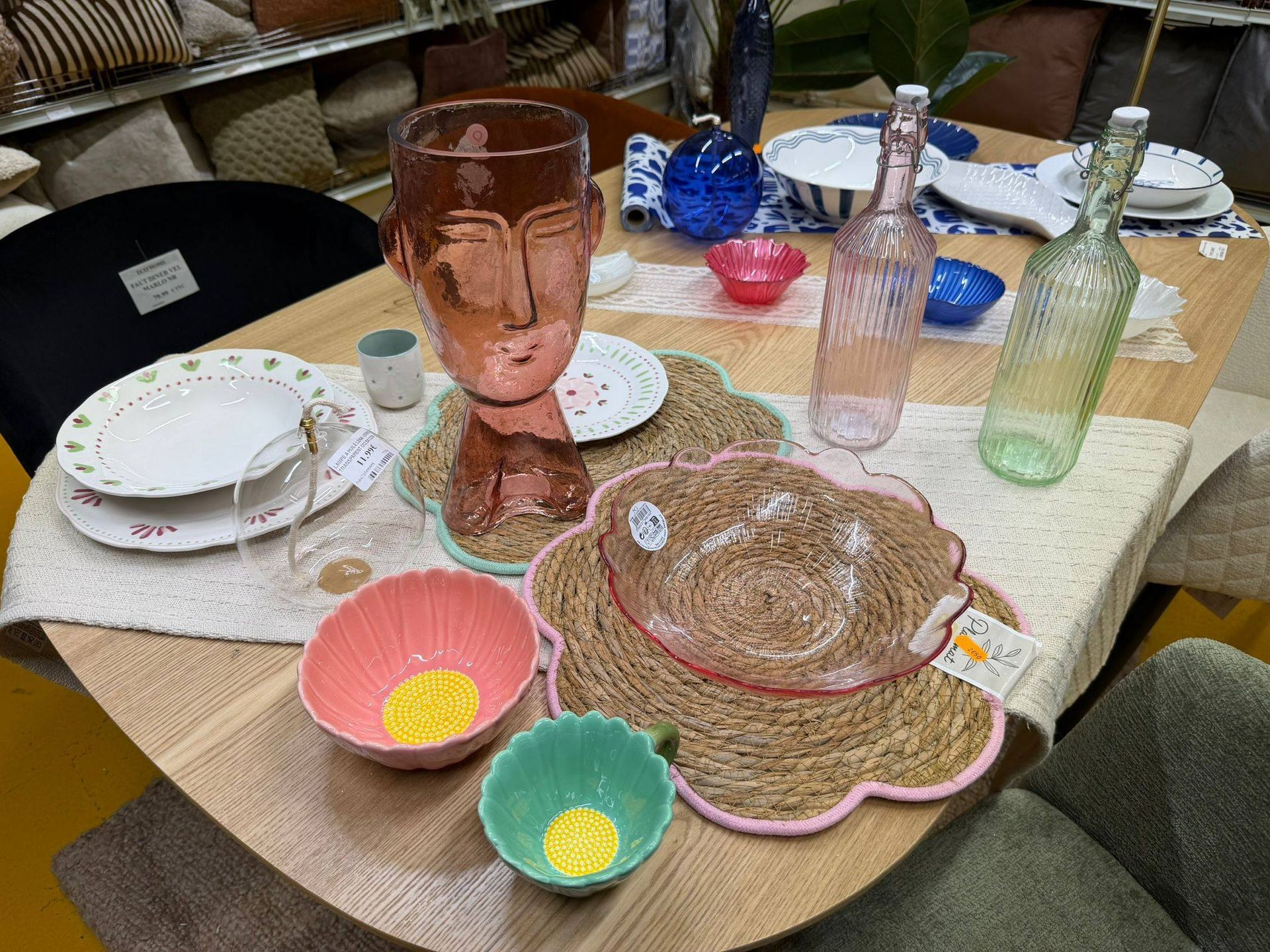 Des verres et des bols colorés sont disposés sur une table à manger avec des assiettes et un set de table à motifs floraux.