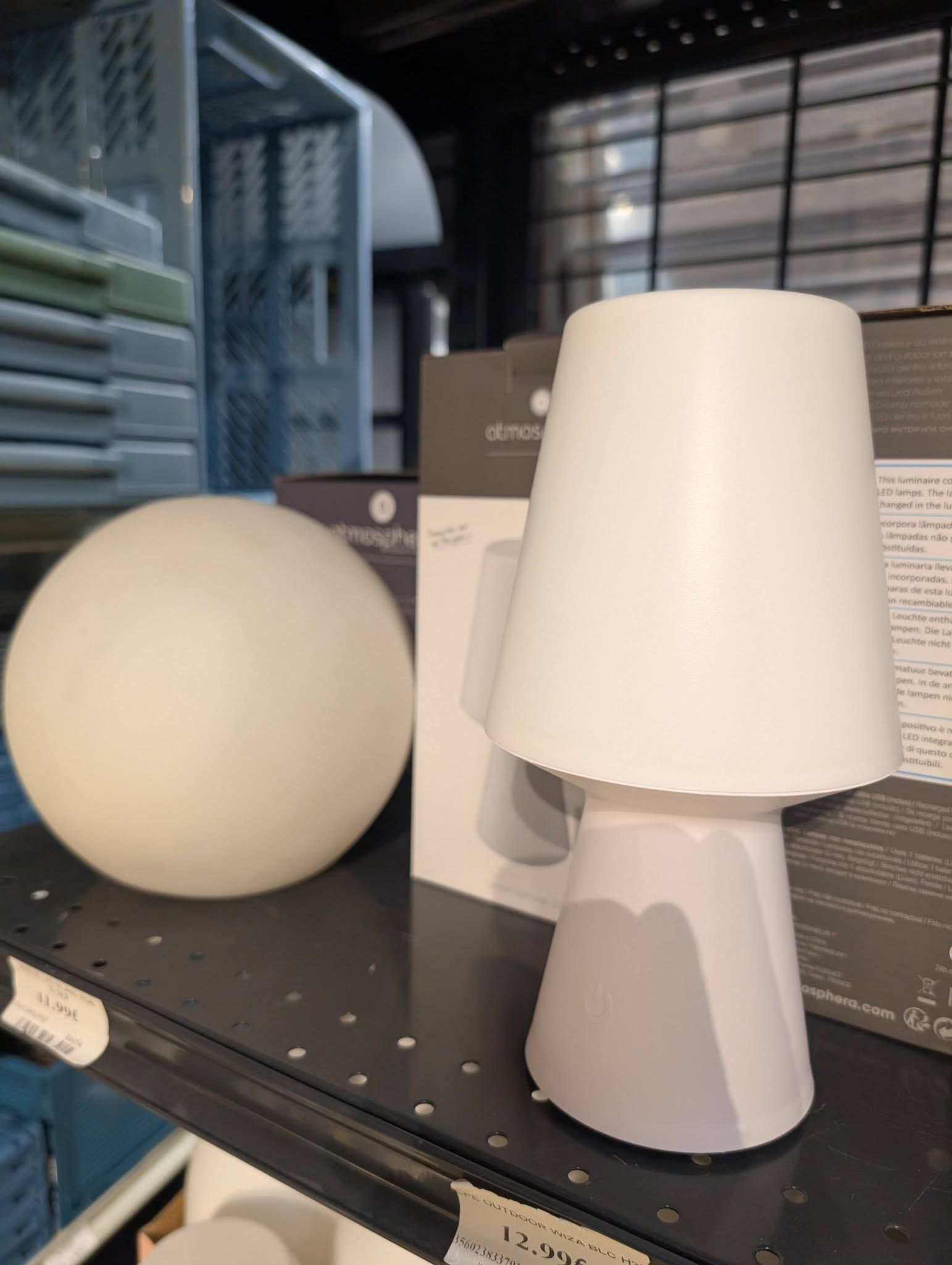 Sphère blanche et lampe conique présentées sur une étagère noire de magasin.