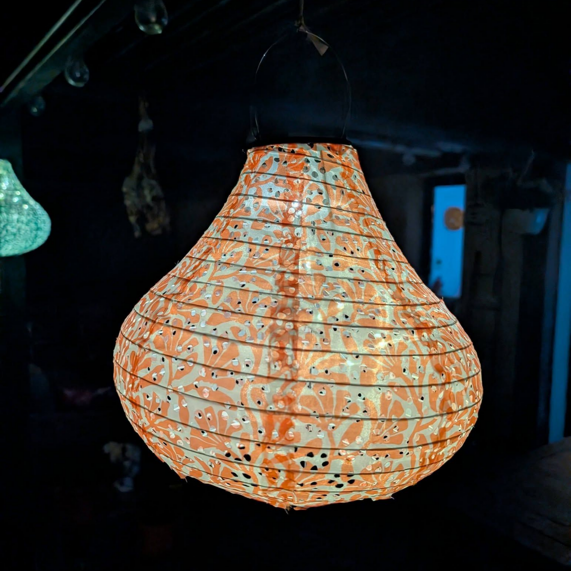 Lanternes suspendues à motifs orange ou verts brillants dans l'obscurité.