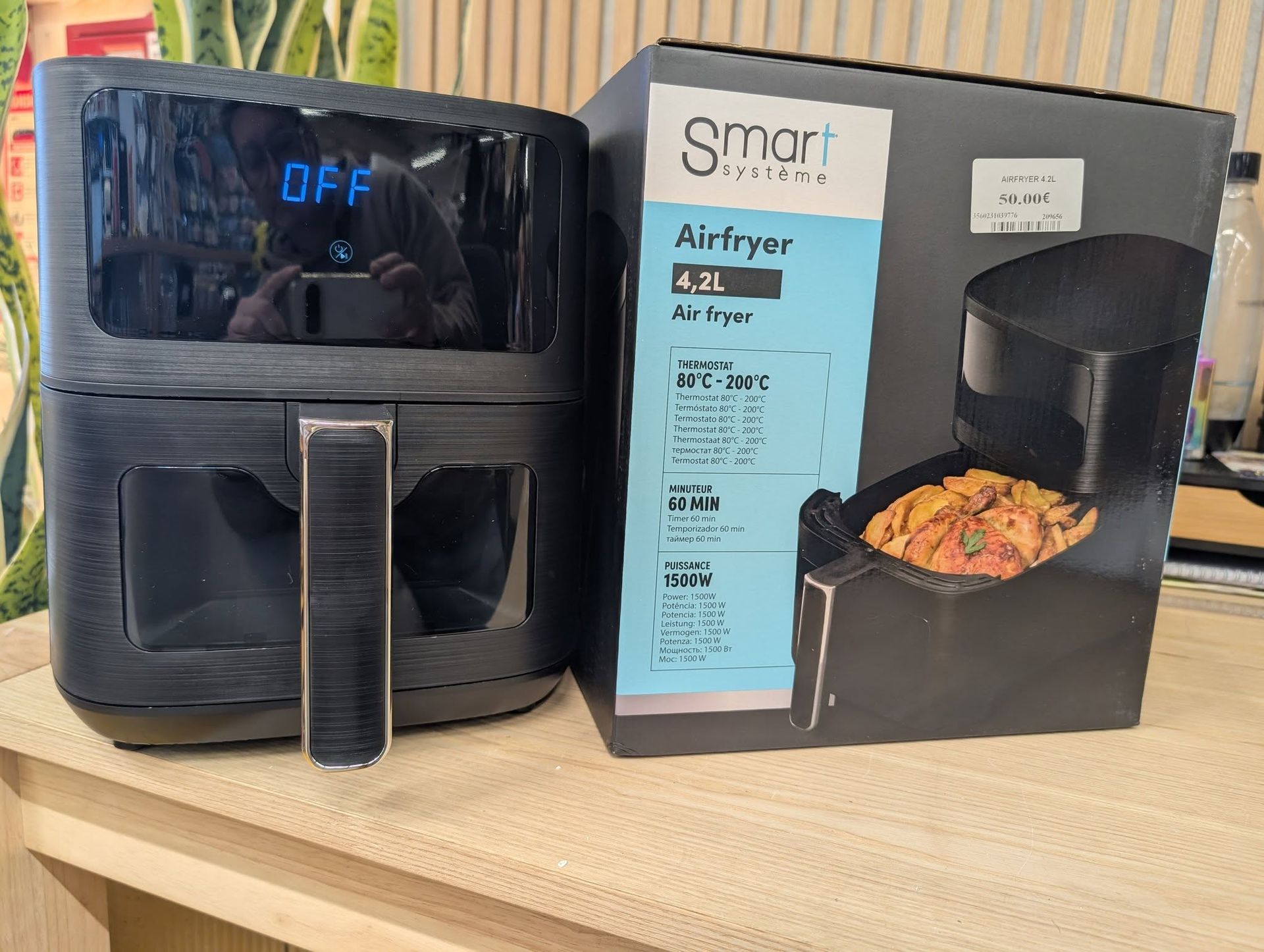 Air fryer noir posé sur le plan de travail à côté de sa boîte, le panier étant partiellement ouvert et contenant des aliments.