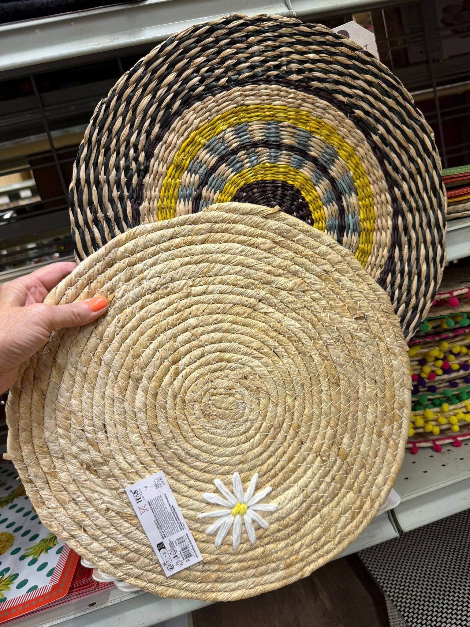 Une main tenant un set de table rond en paille tressée orné d'une fleur blanche.